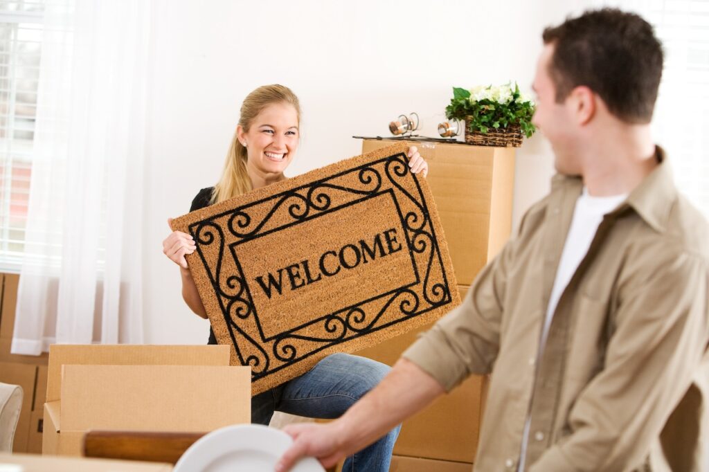 Moving: Woman Holds Welcome Mat On Moving In Day Moving: Woman Holds Welcome Mat On Moving In Day